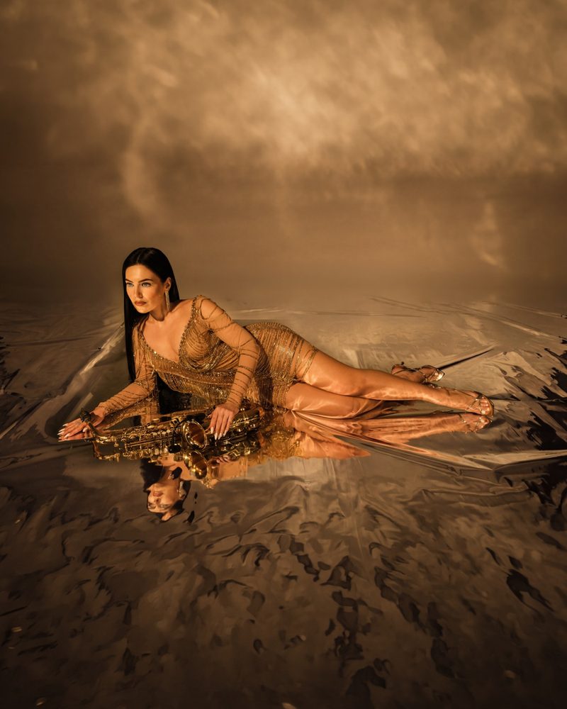 Woman in a gold dress with a saxophone on a mirrored floor