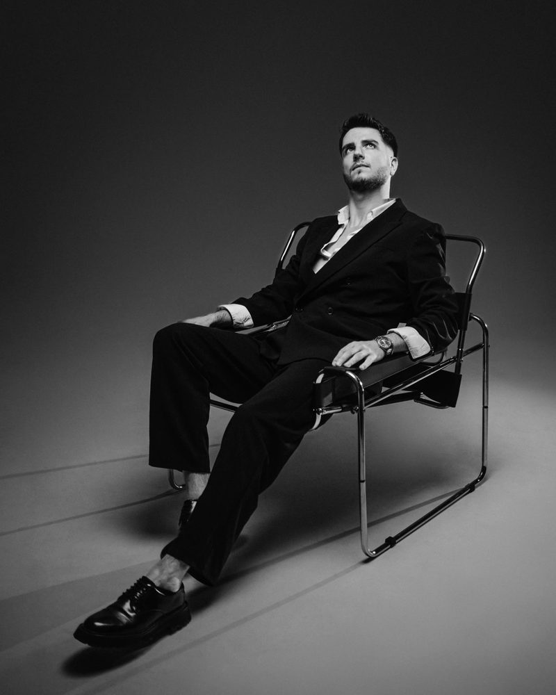 Black-and-white portrait of a man in a suit on a tubular steel chair